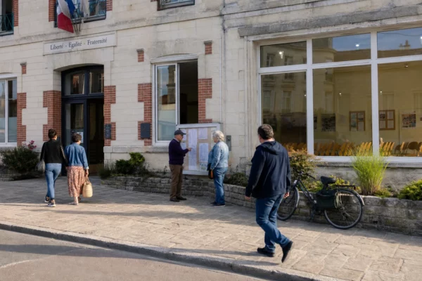 Rue d’une ville moyenne française devant un bâtiment municipal, avec des habitants anonymes dans une lumière claire de fin de journée