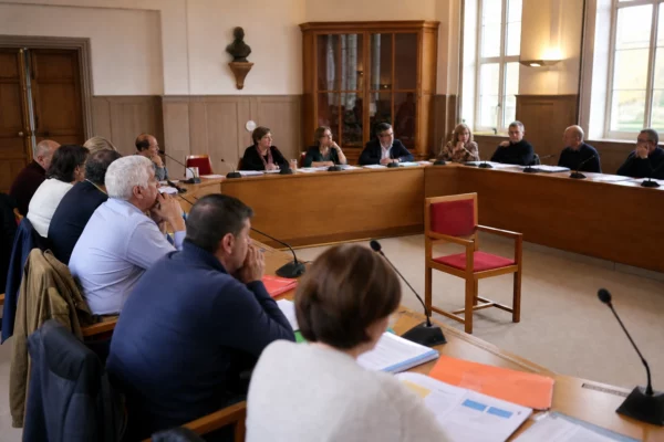 Salle de conseil municipal française avec une chaise vide, des micros et des dossiers sur une table