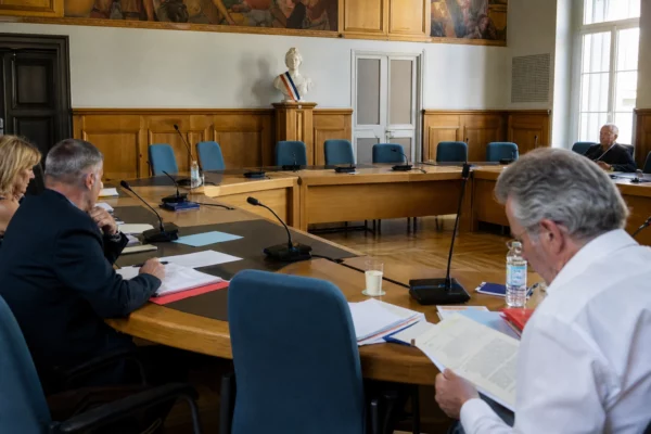 Salle de conseil municipal française avec chaises vides, micros et dossiers avant un débat politique