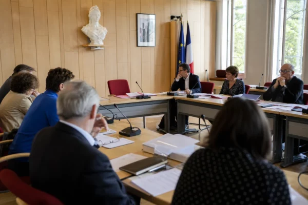 Salle municipale française avec militants anonymes, micros et chaise vide lors d’une réunion politique à Blois