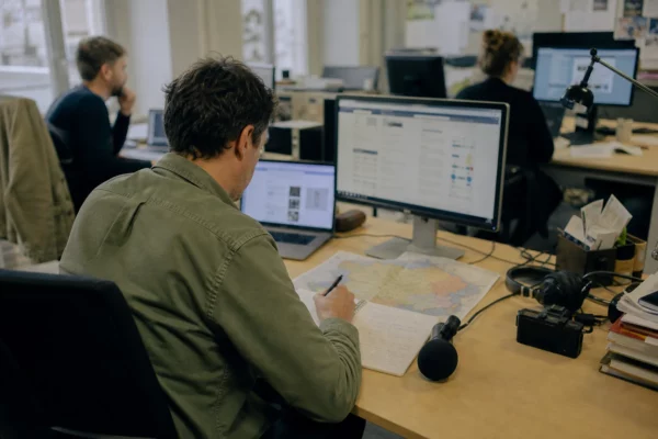 Journaliste préparant un sujet sur la primaire présidentielle dans une rédaction locale française, avec carnet et carte floue