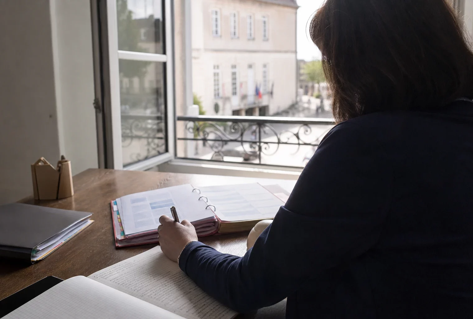 Collaborateur politique anonyme prenant des notes dans un dossier au sein d’une mairie française lumineuse