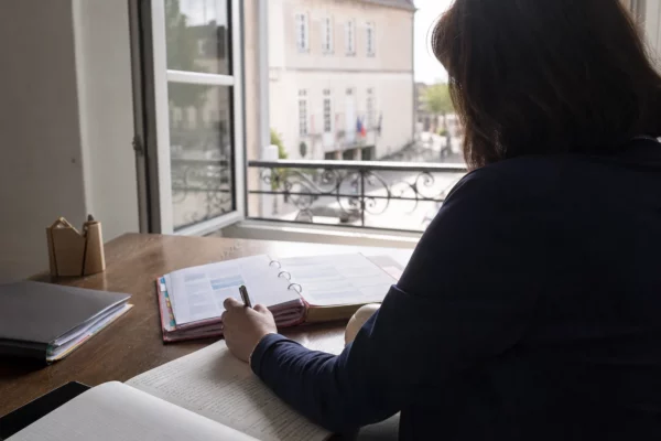 Collaborateur politique anonyme prenant des notes dans un dossier au sein d’une mairie française lumineuse