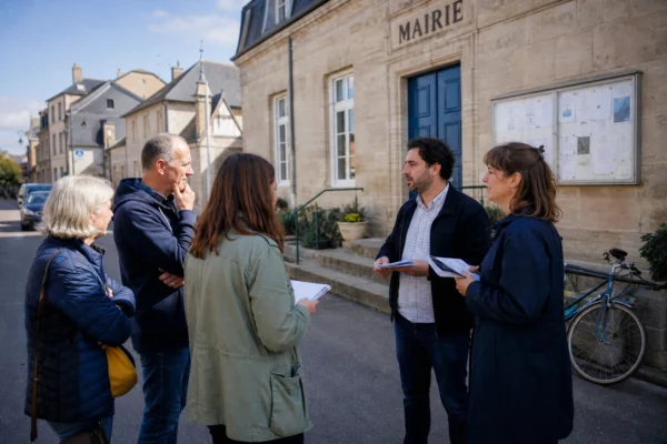 Citoyens anonymes échangeant sur une primaire politique devant une mairie française, en pleine lumière naturelle