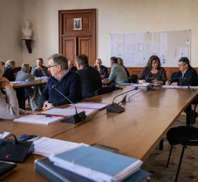 Salle municipale française préparant une réunion politique, avec micros, dossiers flous et une chaise vide