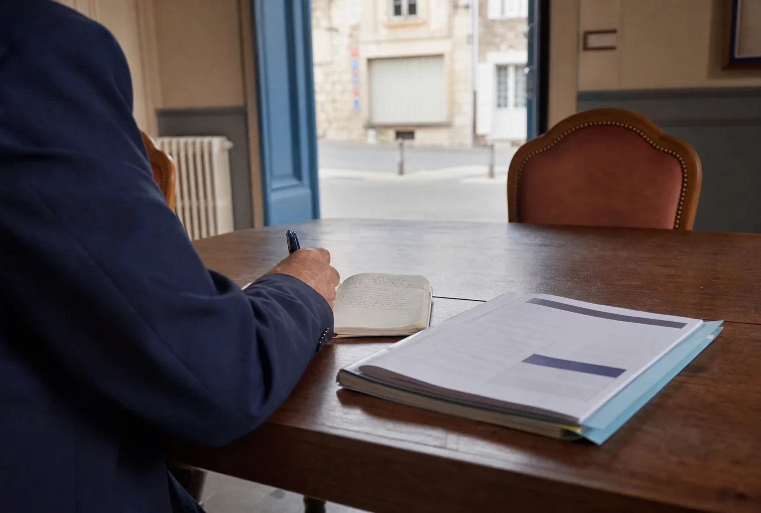 Élu local anonyme prenant des notes dans une mairie française, avec un dossier civique et une rue en arrière-plan