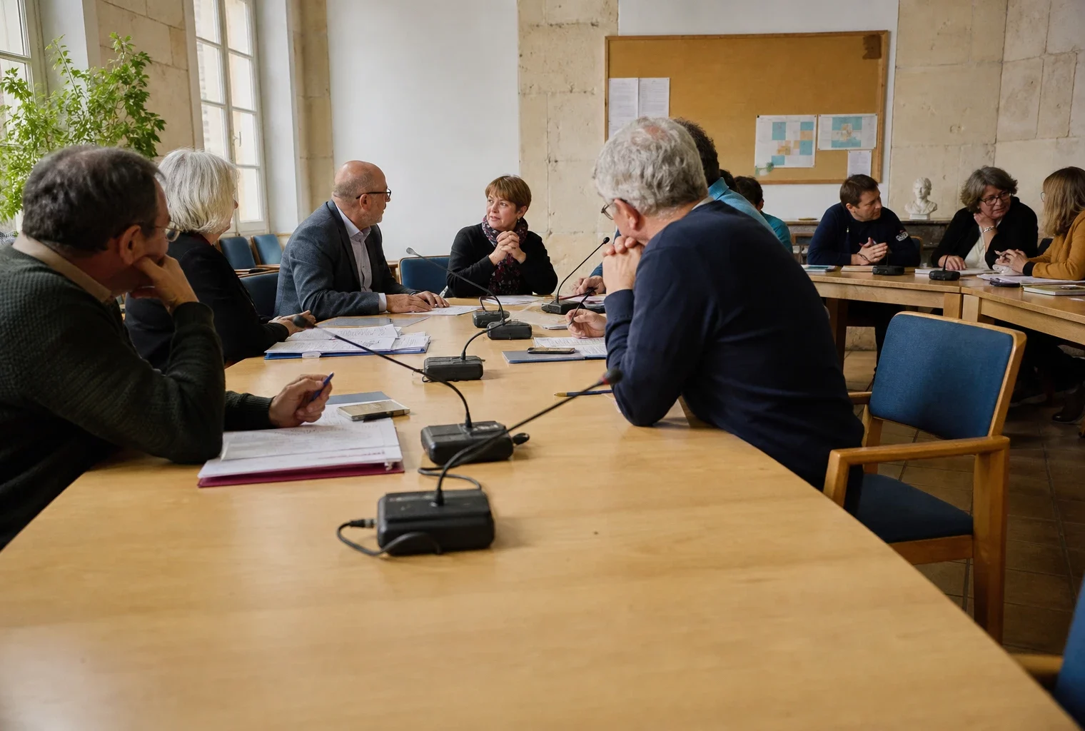 Salle municipale française réunissant des élus anonymes autour de micros, dossiers et d’une chaise vide
