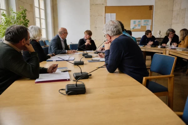 Salle municipale française réunissant des élus anonymes autour de micros, dossiers et d’une chaise vide