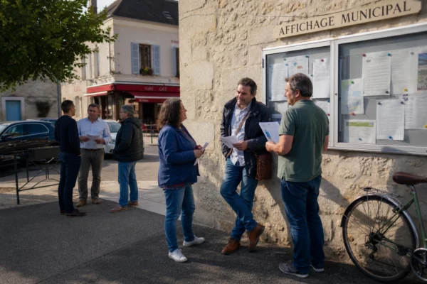 Habitants anonymes discutant sur une place française, près d’un équipement municipal, dans une scène de débat civique