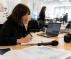 Journaliste en rédaction préparant un sujet sur Ceuta, avec carnet, micro et carte floue sur un bureau lumineux