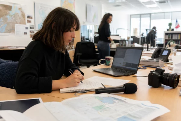 Journaliste en rédaction préparant un sujet sur Ceuta, avec carnet, micro et carte floue sur un bureau lumineux