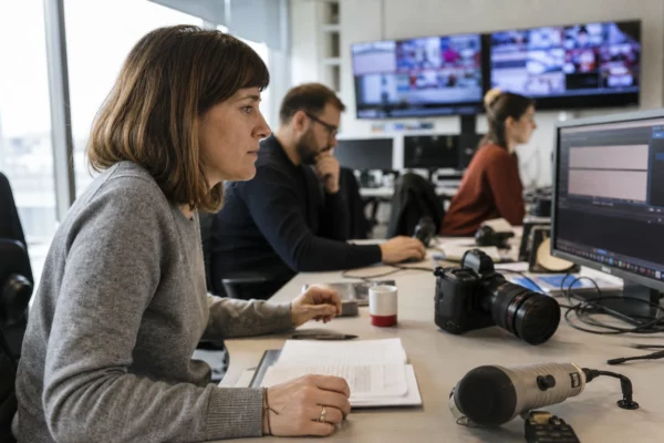 Une rédaction française lumineuse avec journalistes, micros et écrans flous autour d’un sujet de désinformation.