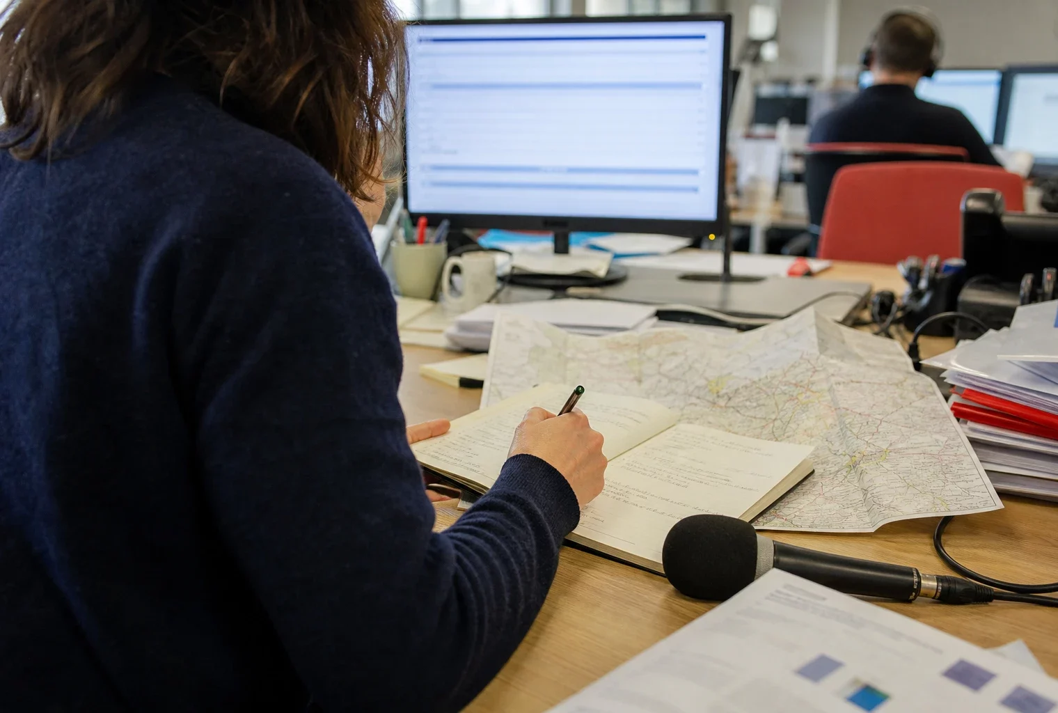 Journaliste préparant un sujet sur l’école dans une rédaction locale, avec carnet, carte papier et micro sans logo