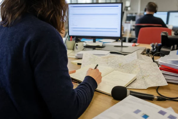 Journaliste préparant un sujet sur l’école dans une rédaction locale, avec carnet, carte papier et micro sans logo