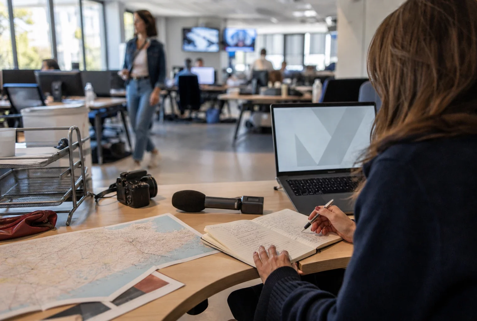 Journaliste préparant un sujet politique territorial dans une rédaction locale française, avec carnet et carte floue