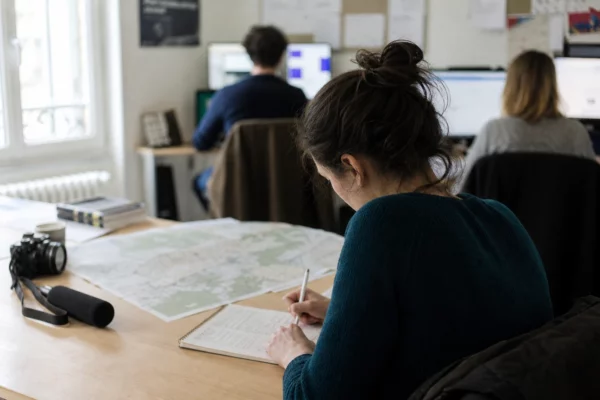 Journaliste préparant une analyse politique dans une rédaction locale française, avec carnet, carte floue et micro de presse