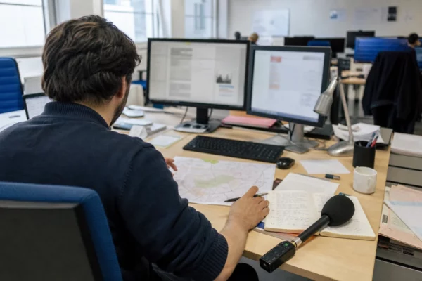 Journaliste préparant un sujet politique local dans une rédaction, avec carnet, carte floue et microphone sans logo
