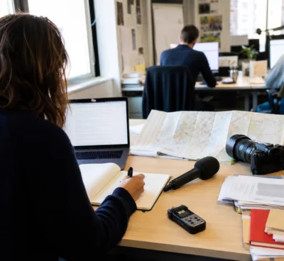 Journaliste préparant un sujet politique dans une rédaction locale française, avec carnet, micro et carte floue