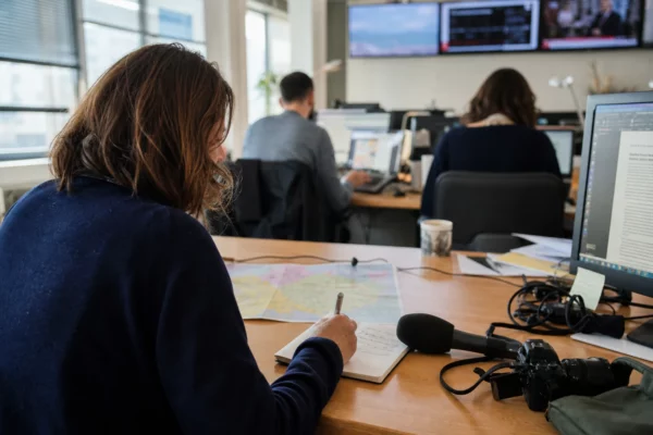 Journaliste préparant un sujet politique dans une rédaction locale française, avec carnet, carte floue et micro sans logo