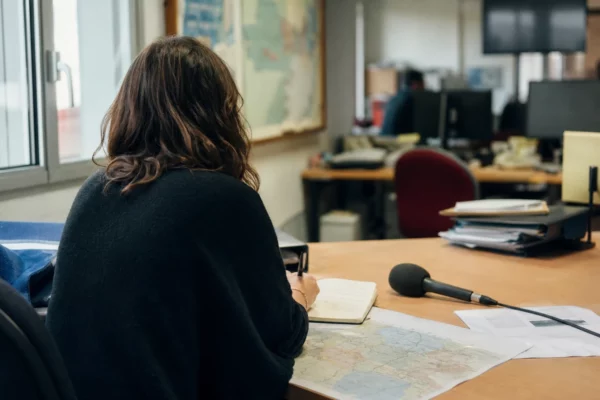Journaliste préparant un sujet dans une rédaction locale française, avec carnet, micro et carte floue sur le bureau