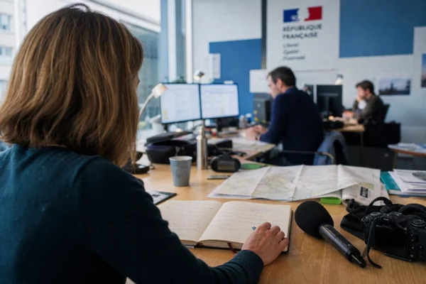 Journaliste préparant un sujet politique dans une rédaction locale française, avec carnet, carte floue et micro sans logo