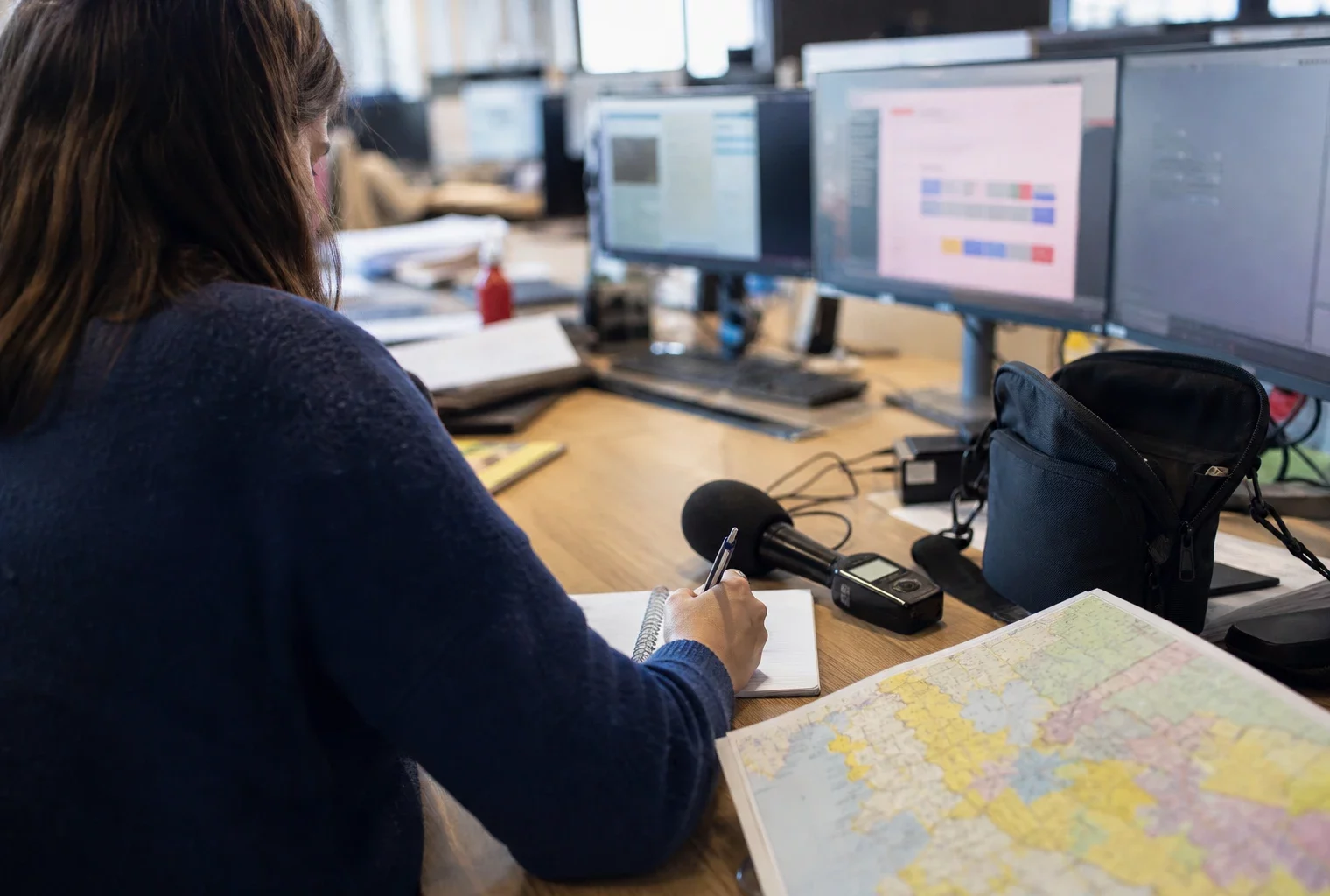 Journaliste préparant un sujet politique dans une rédaction locale française, avec carnet, micro et carte régionale floue