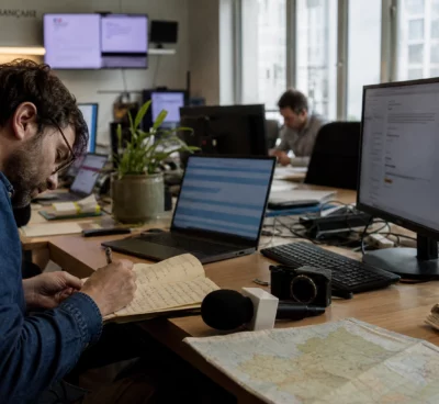 Journaliste préparant une analyse politique dans une rédaction locale française, avec carnet, carte floue et micro de presse