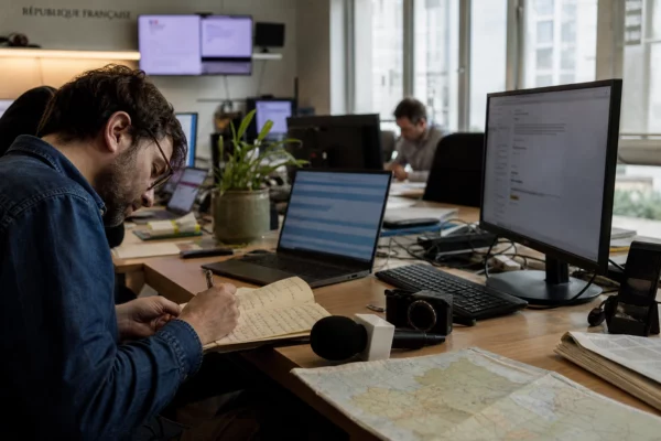 Journaliste préparant une analyse politique dans une rédaction locale française, avec carnet, carte floue et micro de presse