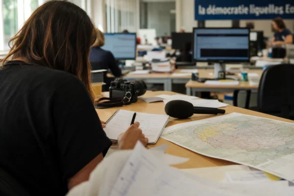 Journaliste préparant un sujet politique local dans une rédaction française, avec carnet, carte floue et micro sans logo