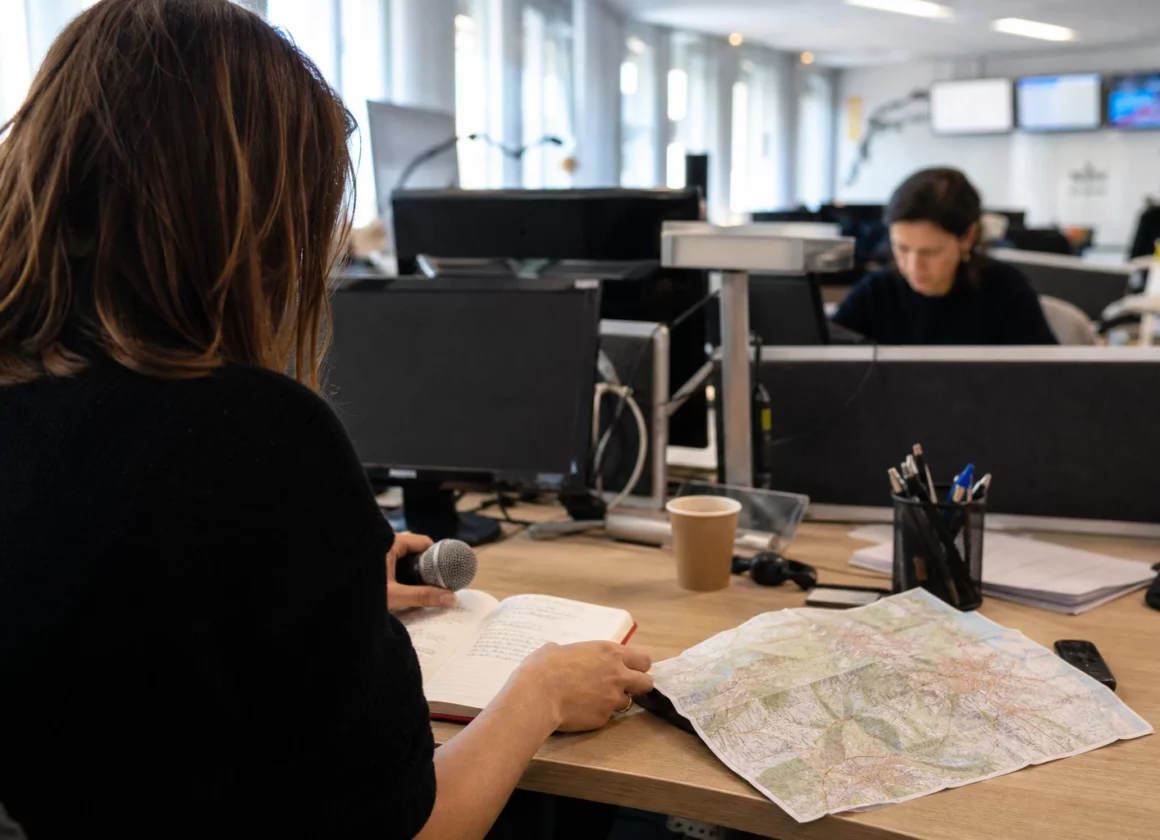 Journaliste préparant un sujet politique dans une rédaction locale à Grenoble, avec carnet, carte floue et micro sans logo