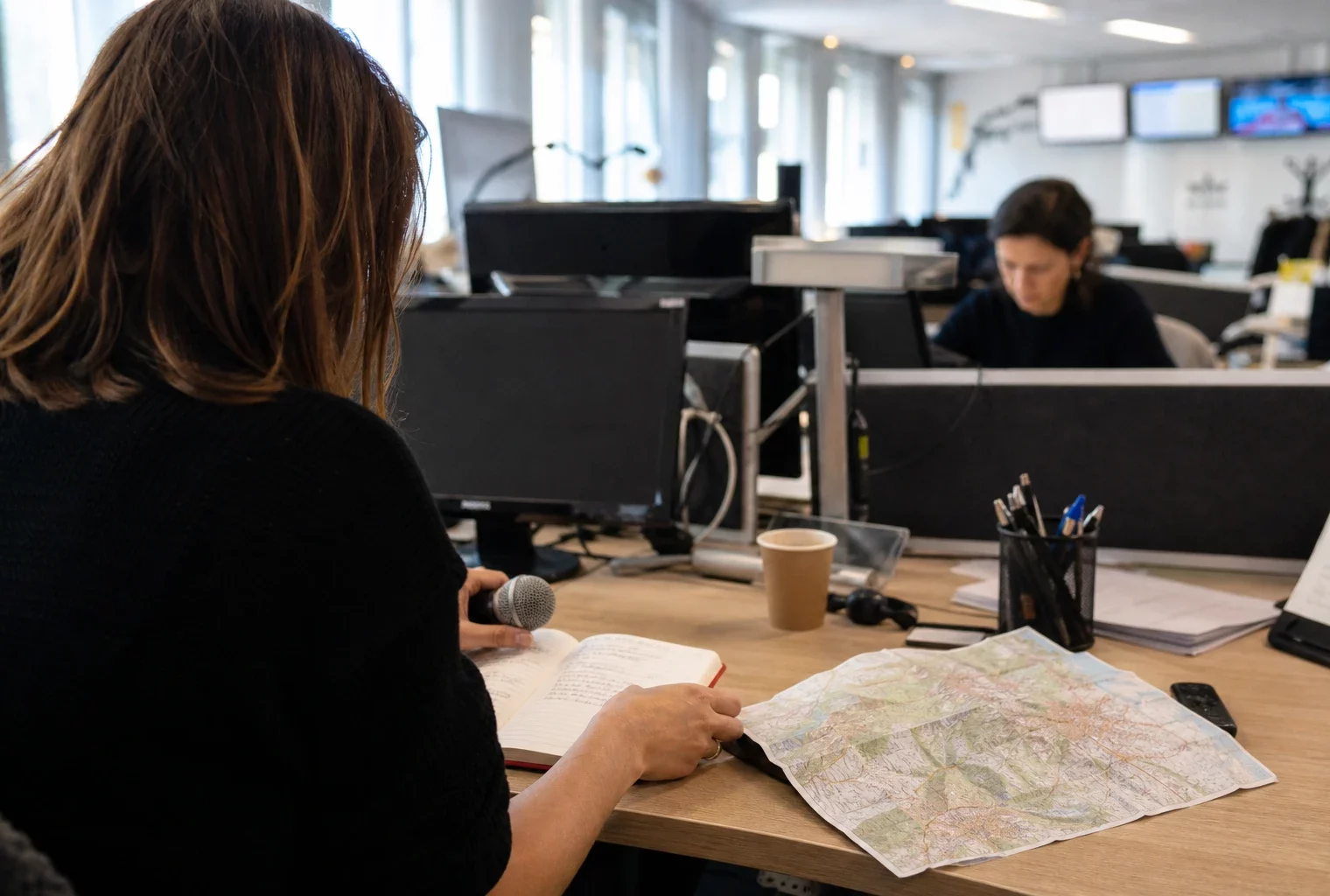 Journaliste préparant un sujet politique dans une rédaction locale à Grenoble, avec carnet, carte floue et micro sans logo