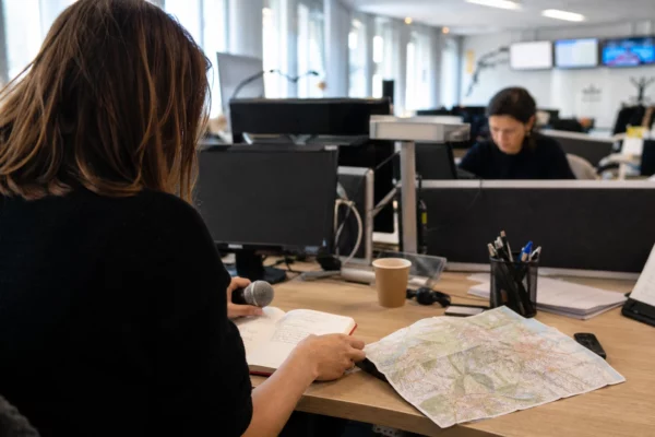 Journaliste préparant un sujet politique dans une rédaction locale à Grenoble, avec carnet, carte floue et micro sans logo