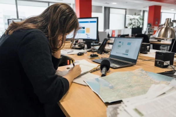Journaliste en rédaction préparant un sujet sur la reconstruction en Gironde, avec carnet, micro et écran flou.