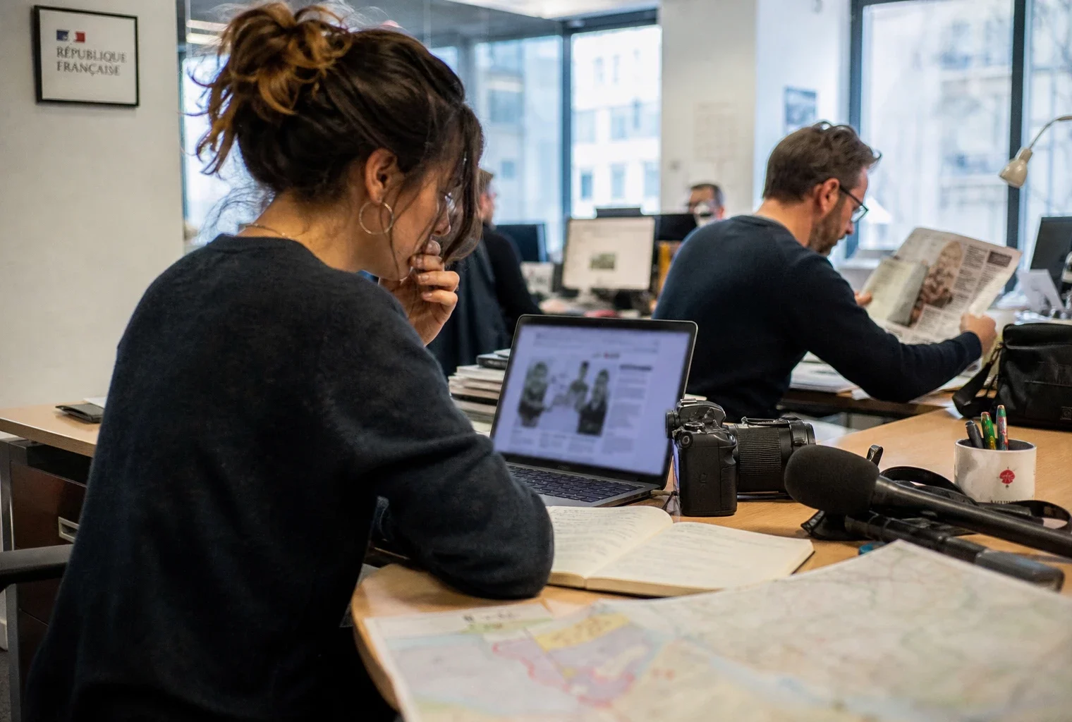 Journaliste dans une rédaction française préparant un sujet territorial avec carnet, micro et carte floue