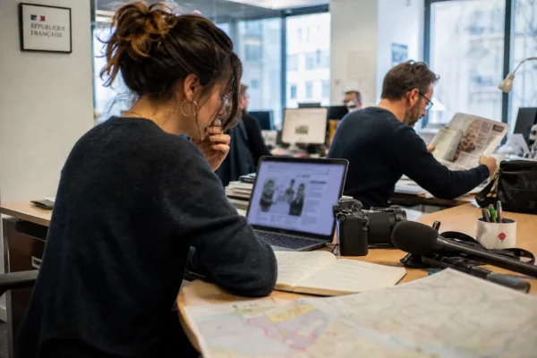 Journaliste dans une rédaction française préparant un sujet territorial avec carnet, micro et carte floue