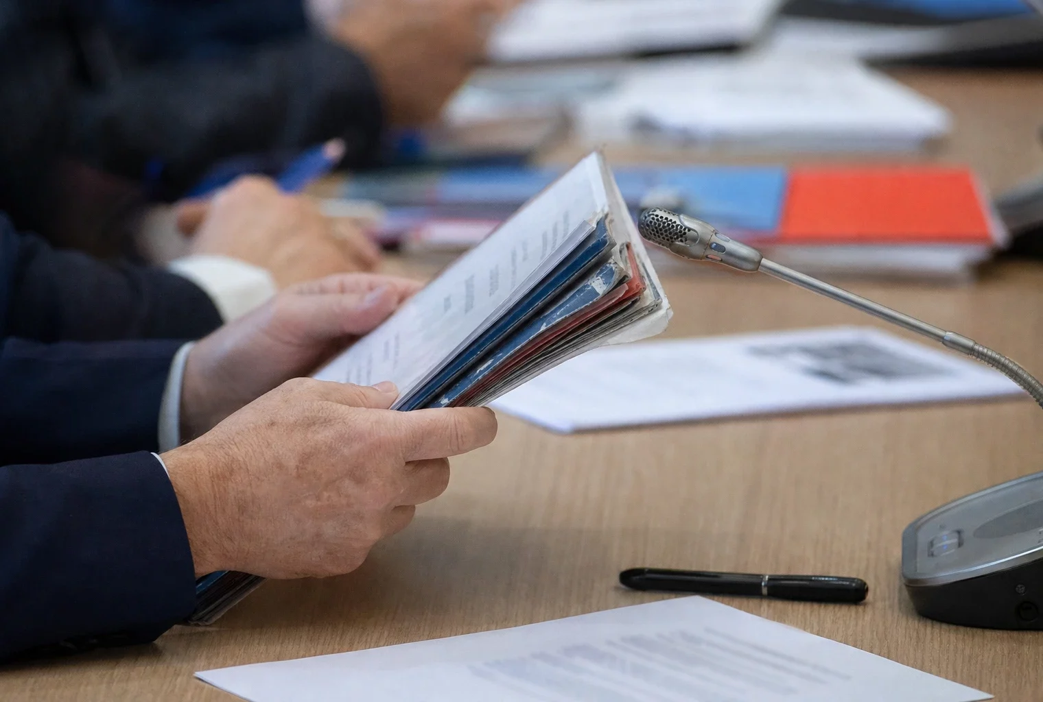 Mains anonymes tenant un dossier lors d’une audition, avec micro de commission et documents flous