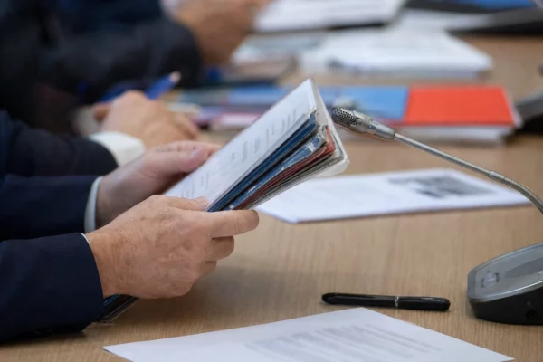 Mains anonymes tenant un dossier lors d’une audition, avec micro de commission et documents flous