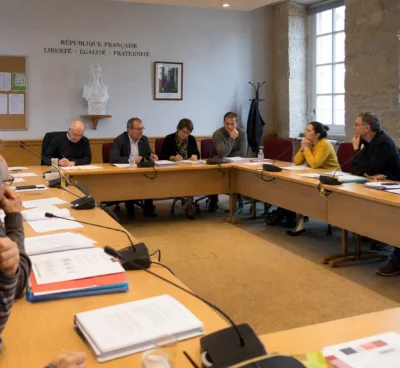 Réunion dans une salle municipale française sur la réforme de la sécurité civile, avec micros, dossiers et une chaise vide