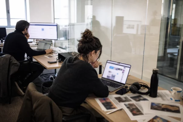 Journaliste et analyste dans une newsroom parisienne, avec écran flou et documents de vérification sur la table.