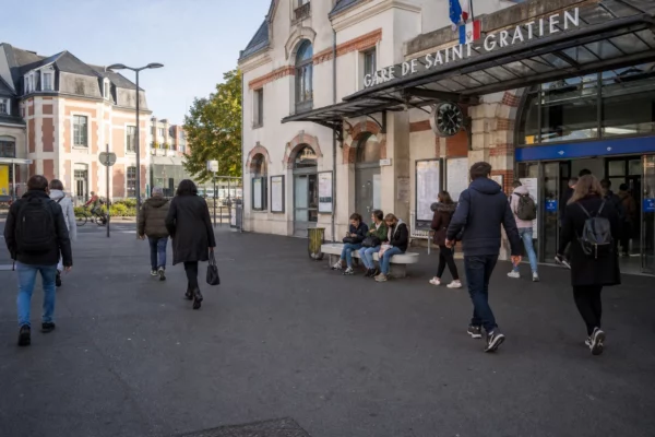 Entrée d’une gare de banlieue française avec des usagers anonymes et une ambiance de quartier en journée.