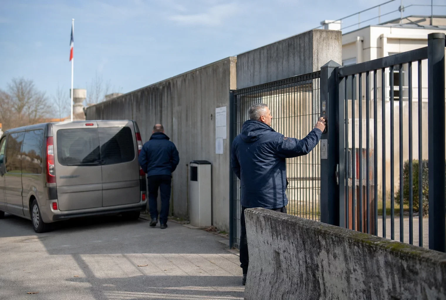 Scène de reportage devant un bâtiment institutionnel français, avec deux agents anonymes et un véhicule utilitaire banal.