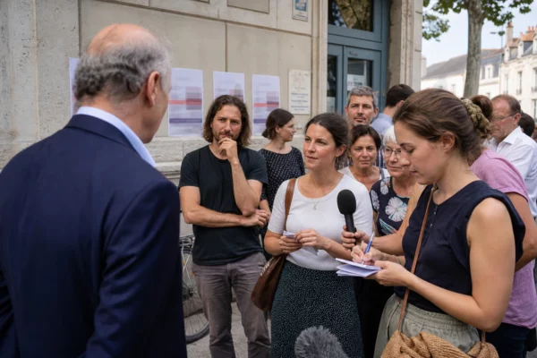 Scène de rue à Blois avec un ancien responsable politique échangeant avec des habitants et des journalistes anonymes