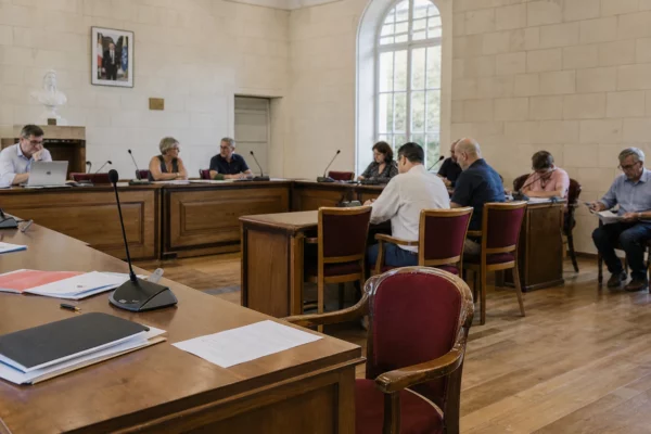 Salle de conseil municipale en France, avec chaise vide, micros et dossiers flous dans une lumière naturelle claire.
