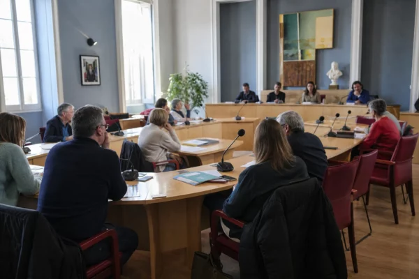 Salle municipale française avec chaise vide, micros et dossiers lors d’un conseil local sous tension numérique