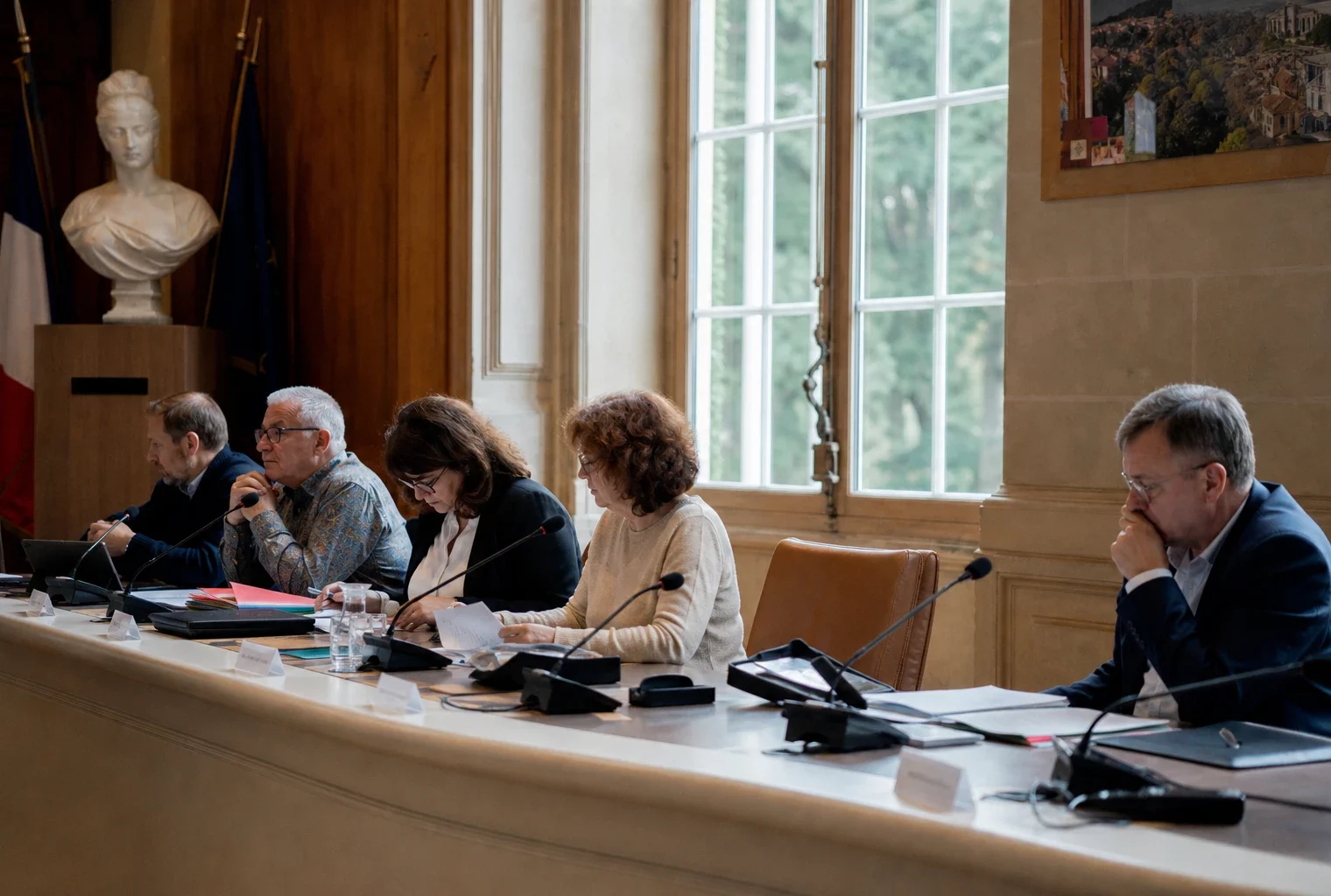 Salle municipale française avec chaise vide, micros et dossiers sur une table, en ambiance de conseil local