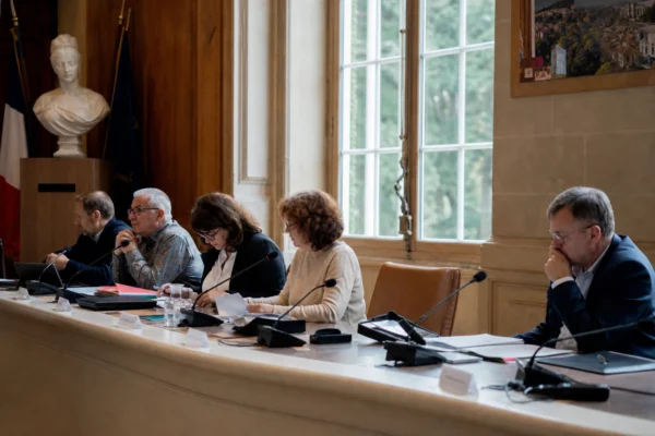 Salle municipale française avec chaise vide, micros et dossiers sur une table, en ambiance de conseil local