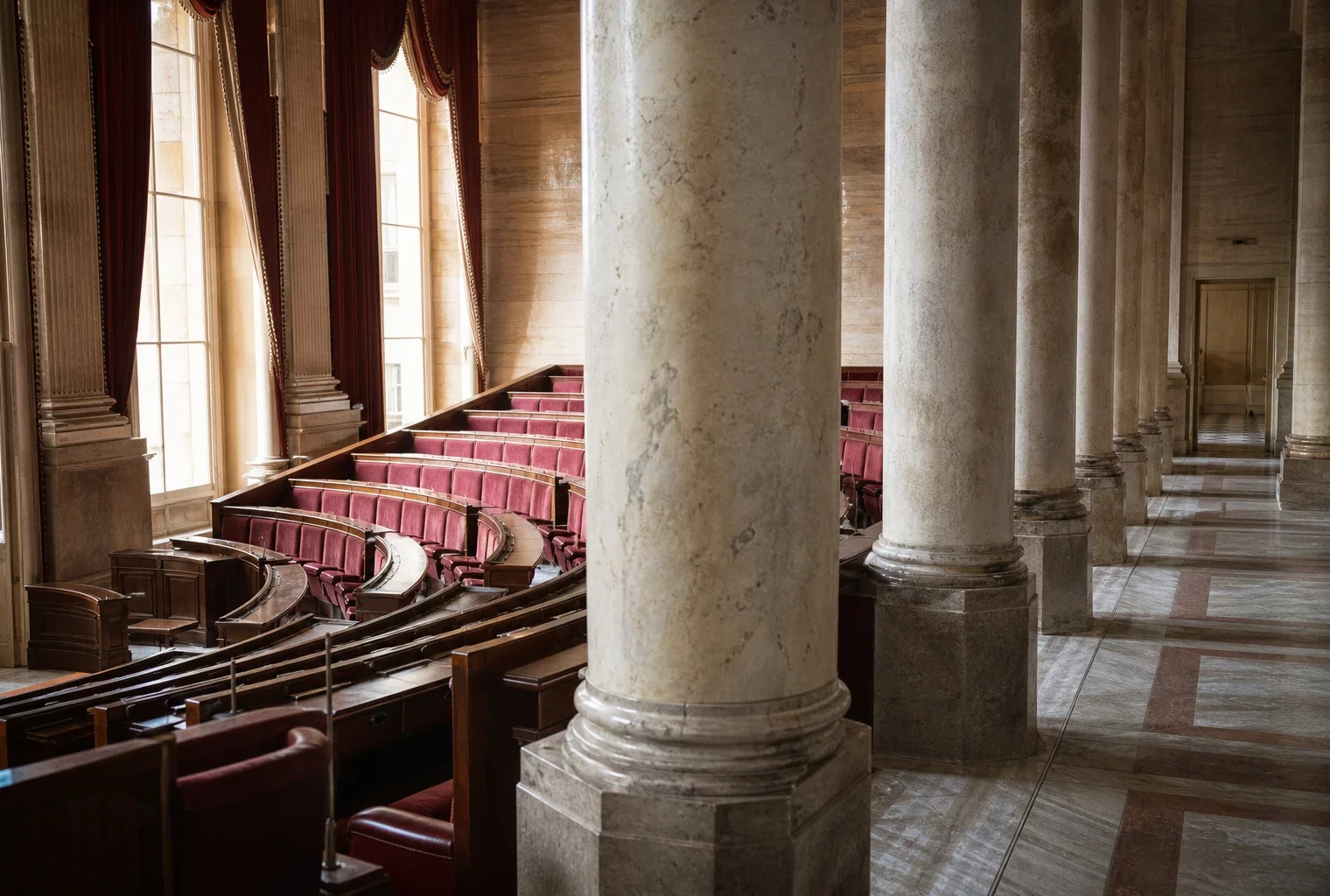 Salle des Quatre-Colonnes de l’Assemblée nationale, vide, avec marbre clair et sièges rouges sous la lumière du jour.