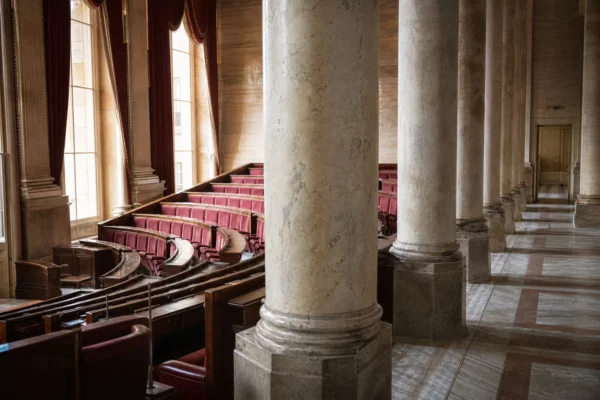Salle des Quatre-Colonnes de l’Assemblée nationale, vide, avec marbre clair et sièges rouges sous la lumière du jour.