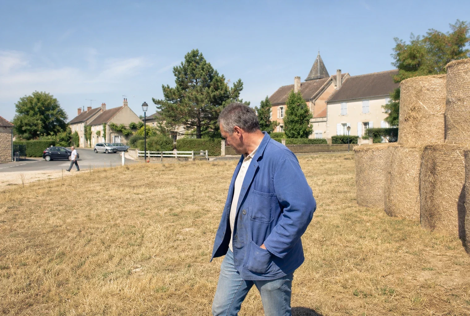 Agriculteur inspectant une prairie sèche près d’un village français pendant une période de sécheresse