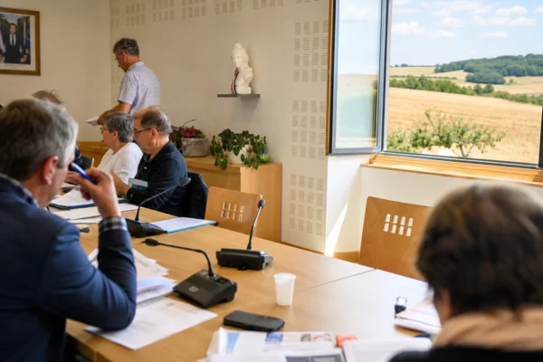 Salle de conseil local dans le Grand Est, avec micros, dossiers flous et une chaise vide face aux enjeux agricoles